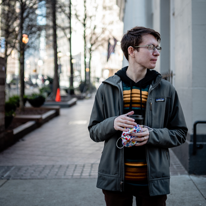 Eliot standing next to a tall building, with coffee.